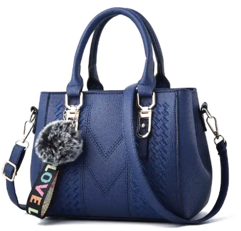 Bleu marine profond, le sac trapèze aligne ses surpiqûres en chevron et son pompon gris