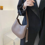 Tenu à la main devant un manteau noir, le hobo taupe grisé et sa sangle réglable argentée