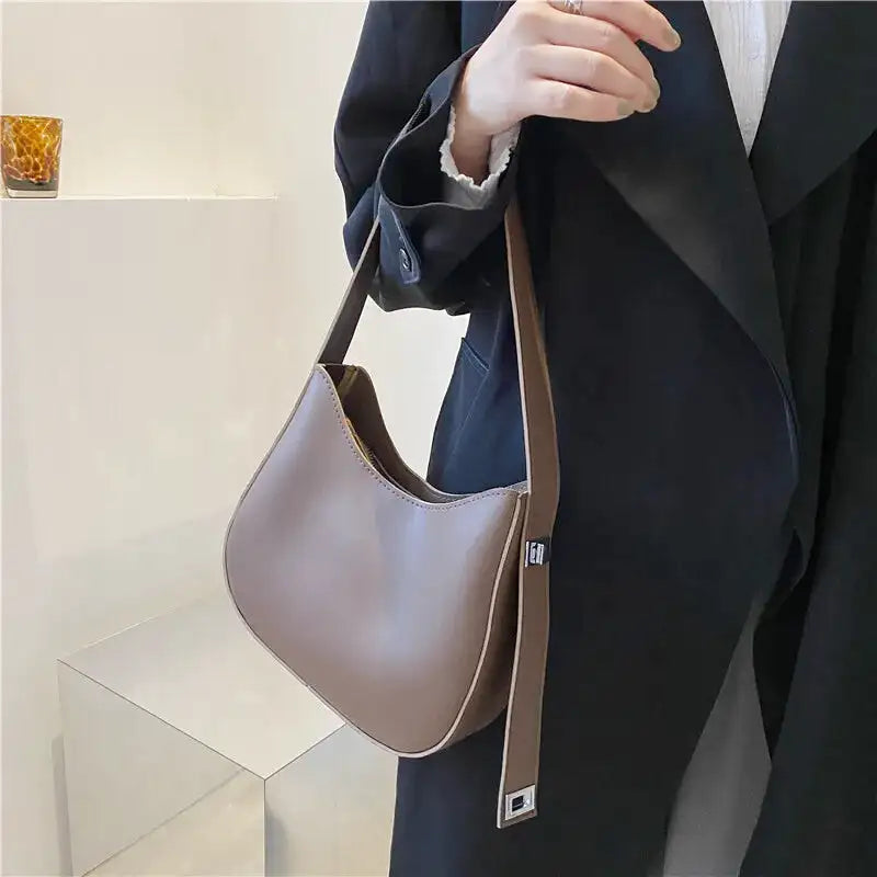 Tenu à la main devant un manteau noir, le hobo taupe grisé et sa sangle réglable argentée