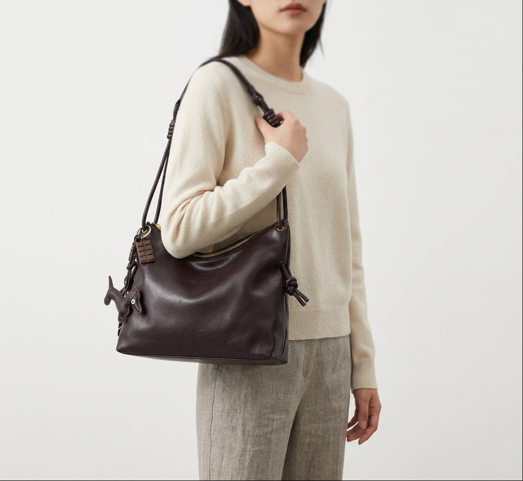 Portée à l'épaule sur un pull écru, la besace brun foncé tombe juste au-dessus de la hanche