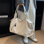 Tenu à la main par ses anses, sac écru volumineux devant un manteau clair et des baskets blanches