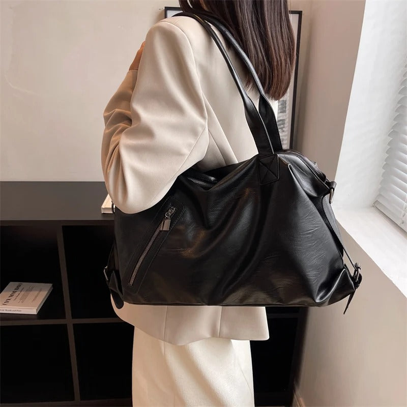 Porté à l'épaule sur un trench beige, le grand sac noir souple s'affaisse sous son propre poids
