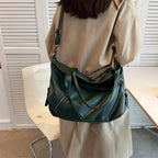 Bandoulière passée en travers du dos, le sac vert foncé repose sur la hanche d'une silhouette en beige