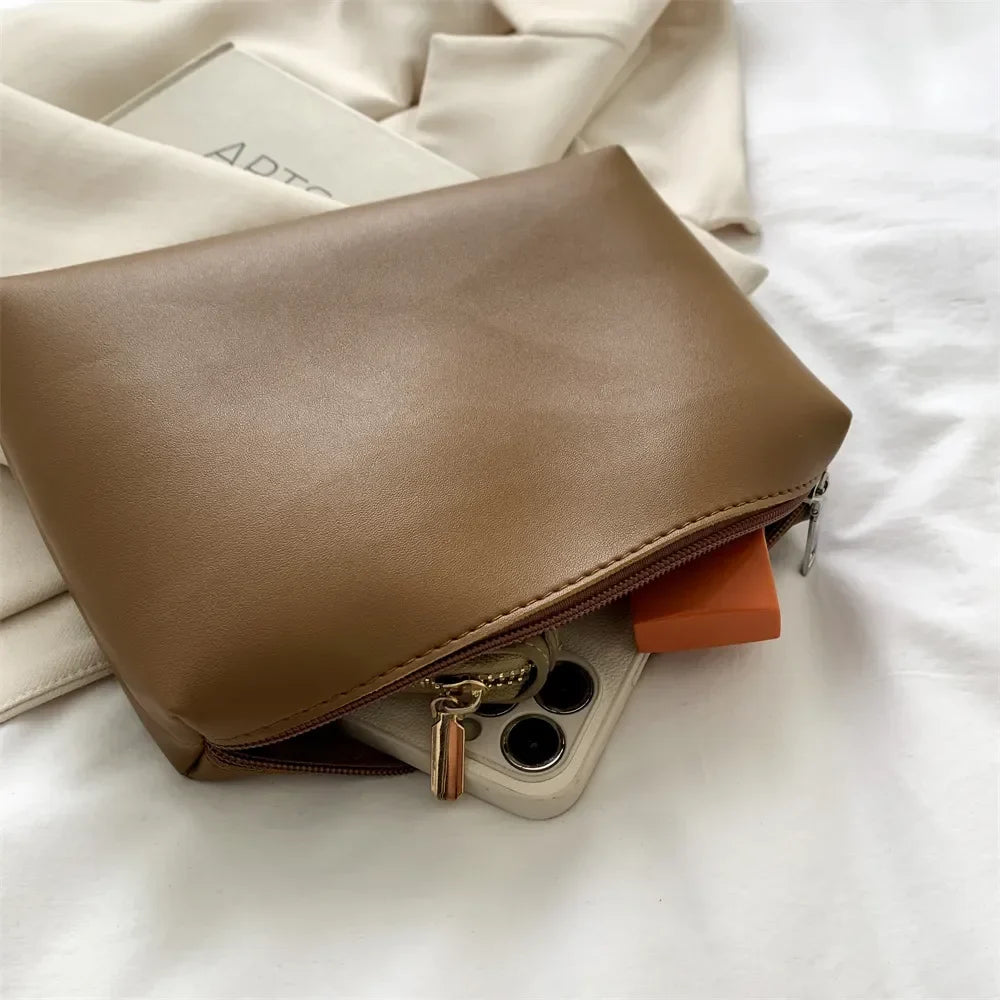 Pochette zippée camel assortie, téléphone glissé dans l'ouverture et tirette dorée en gros plan