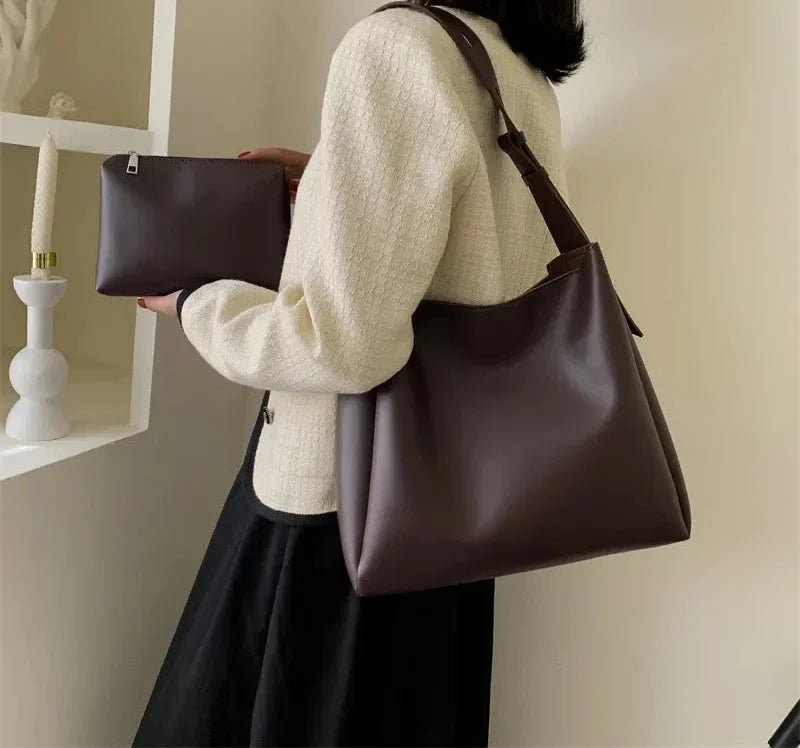 Sac prune porté à l'épaule avec une veste crème, la pochette zippée assortie tenue en main
