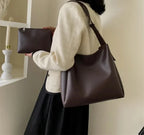 Sac prune porté à l'épaule avec une veste crème, la pochette zippée assortie tenue en main