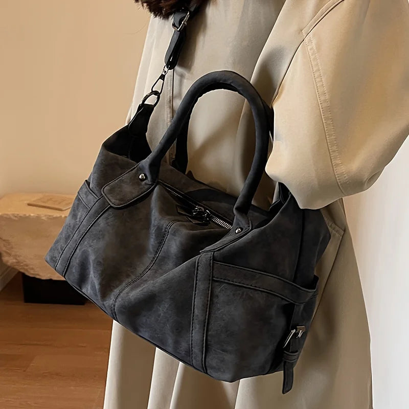 Tenu à la main devant un trench beige, le sac gris anthracite ouvre largement son entrée zippée
