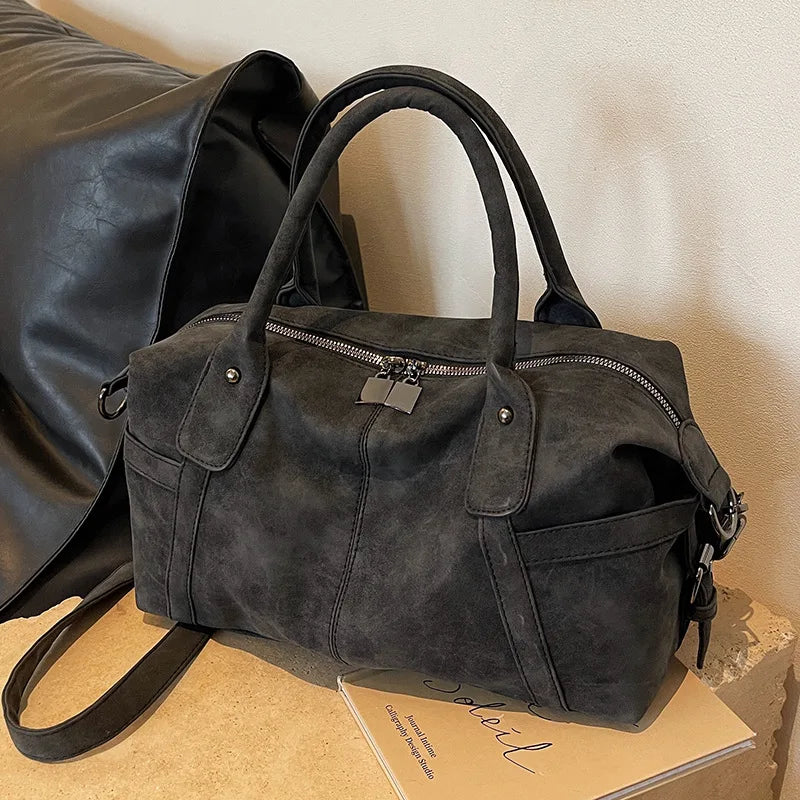 Modèle gris anthracite de trois quarts sur un socle clair, sangle d'épaule pendante et zip fermé