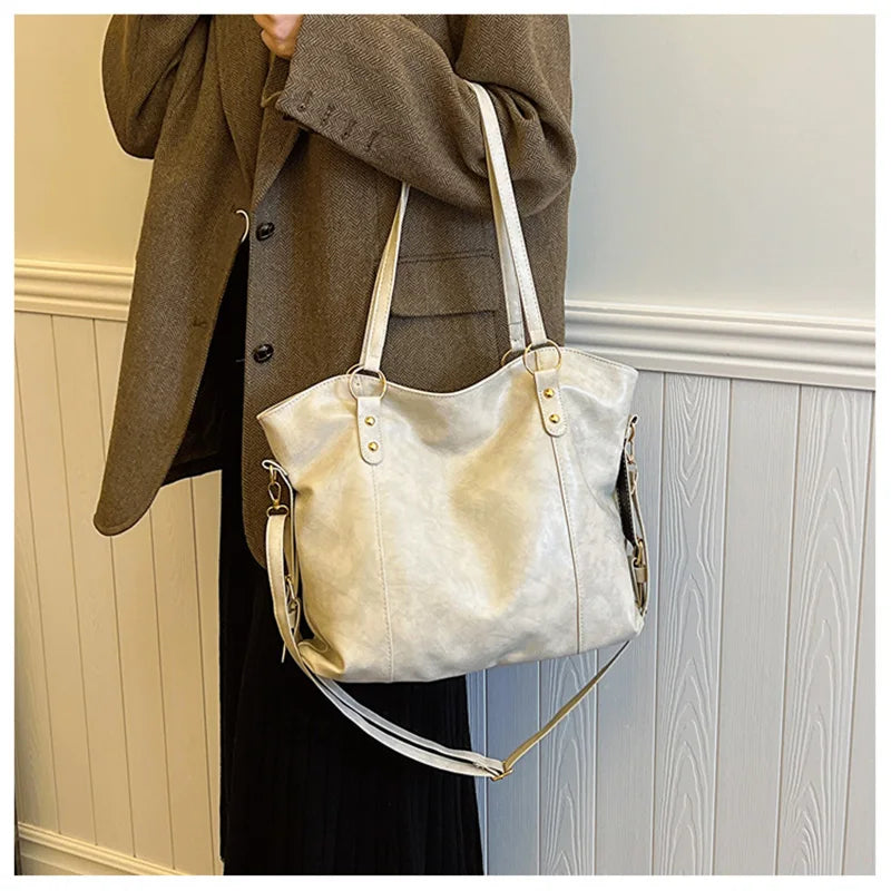 Sur un manteau brun olive et une jupe noire, le cabas écru pend à l'épaule, sangle latérale visible