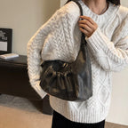 Tenu à l'épaule sur un pull torsadé crème, le hobo brun foncé garde sa silhouette en croissant