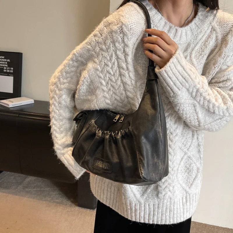 Tenu à l'épaule sur un pull torsadé crème, le hobo brun foncé garde sa silhouette en croissant