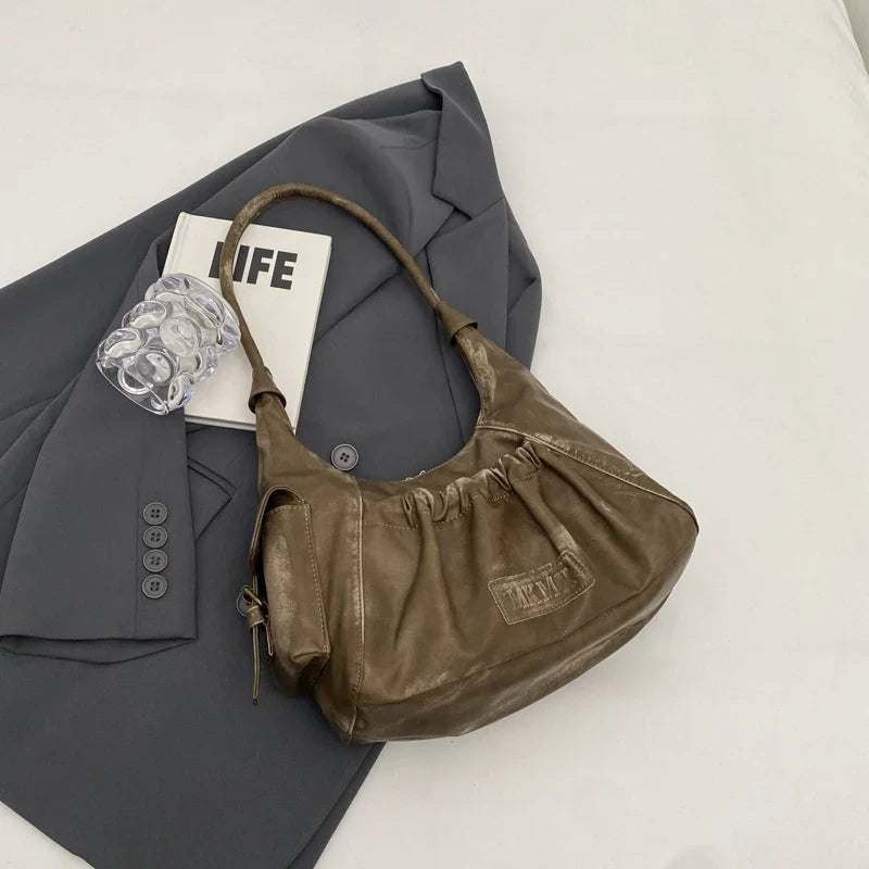 Brun kaki foncé, ce sac croissant montre ses fronces élastiquées et sa patte estampée en relief