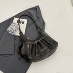 Posé sur une veste grise, le hobo noir patiné dévoile sa poche zippée et sa base arrondie