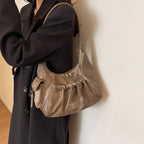 Sous le bras et sur un long manteau sombre, le hobo taupe clair laisse voir sa poche zippée