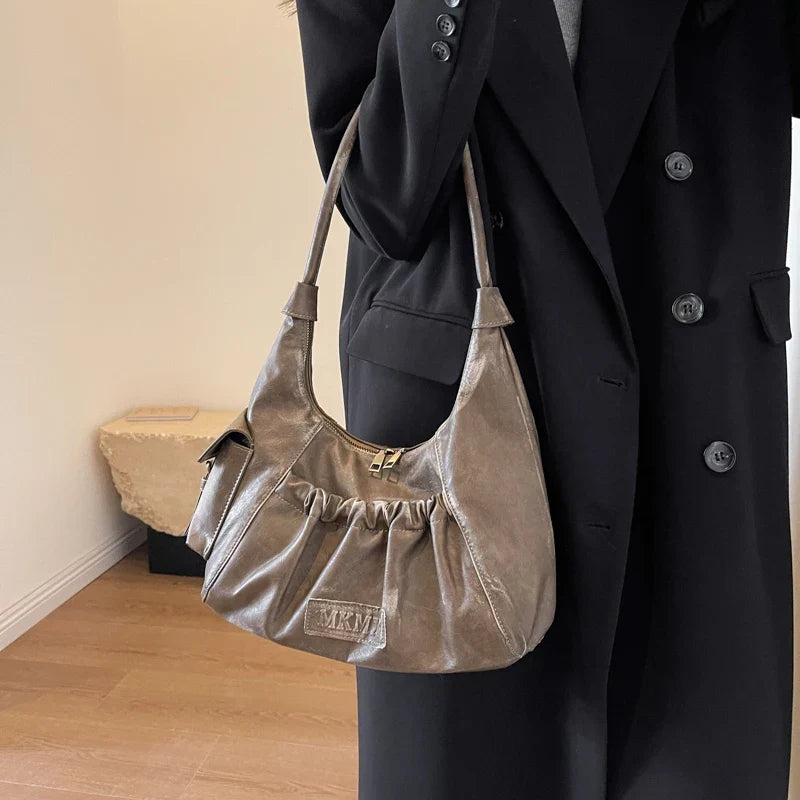 Sur un manteau noir, le sac taupe patiné se cale sous le bras, anse courte passée à l'épaule