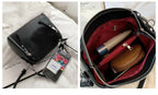 Besace noire posée près d'un téléphone et son intérieur doublé de rouge garni d'accessoires