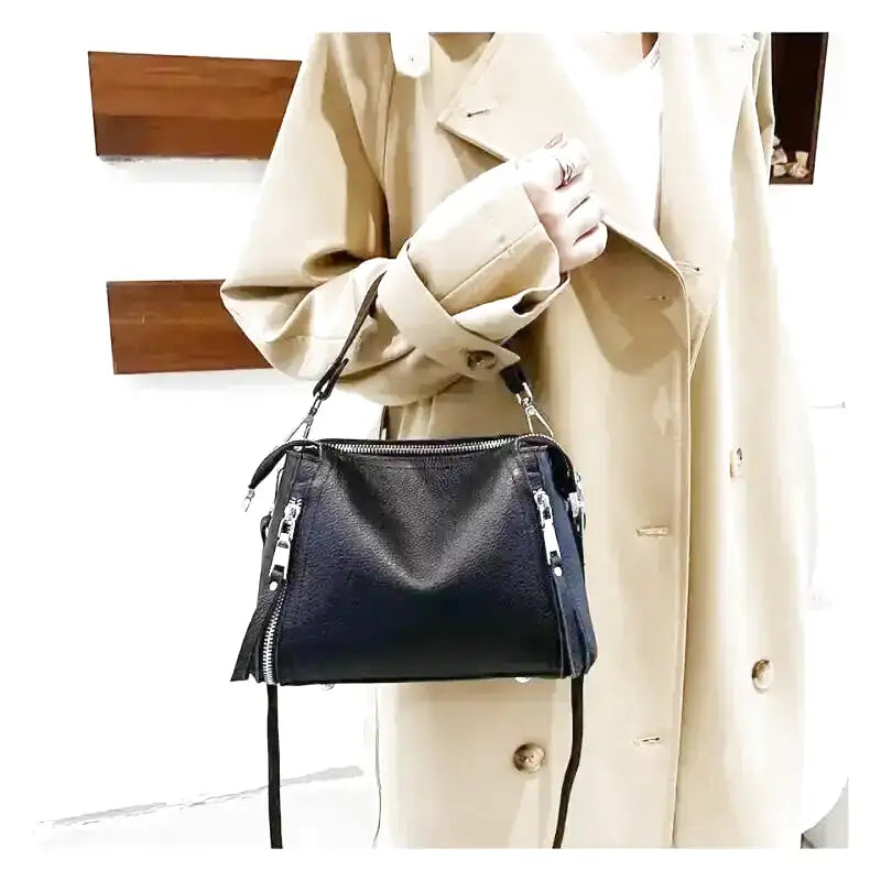 Silhouette en trench beige tenant la besace noire, bandoulière fine retombant librement
