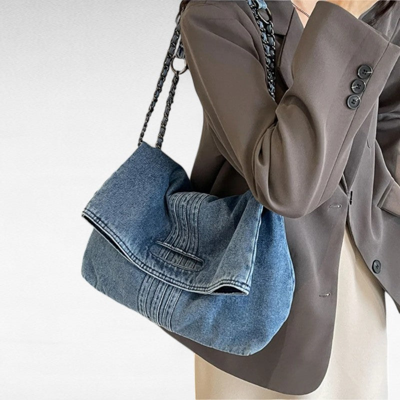 Chaîne tressée sur l'épaule, le sac en denim clair se cale contre un blazer taupe boutonné