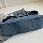 Base plate et large soufflet de la besace en denim posée sur un drap clair, rabat entrouvert