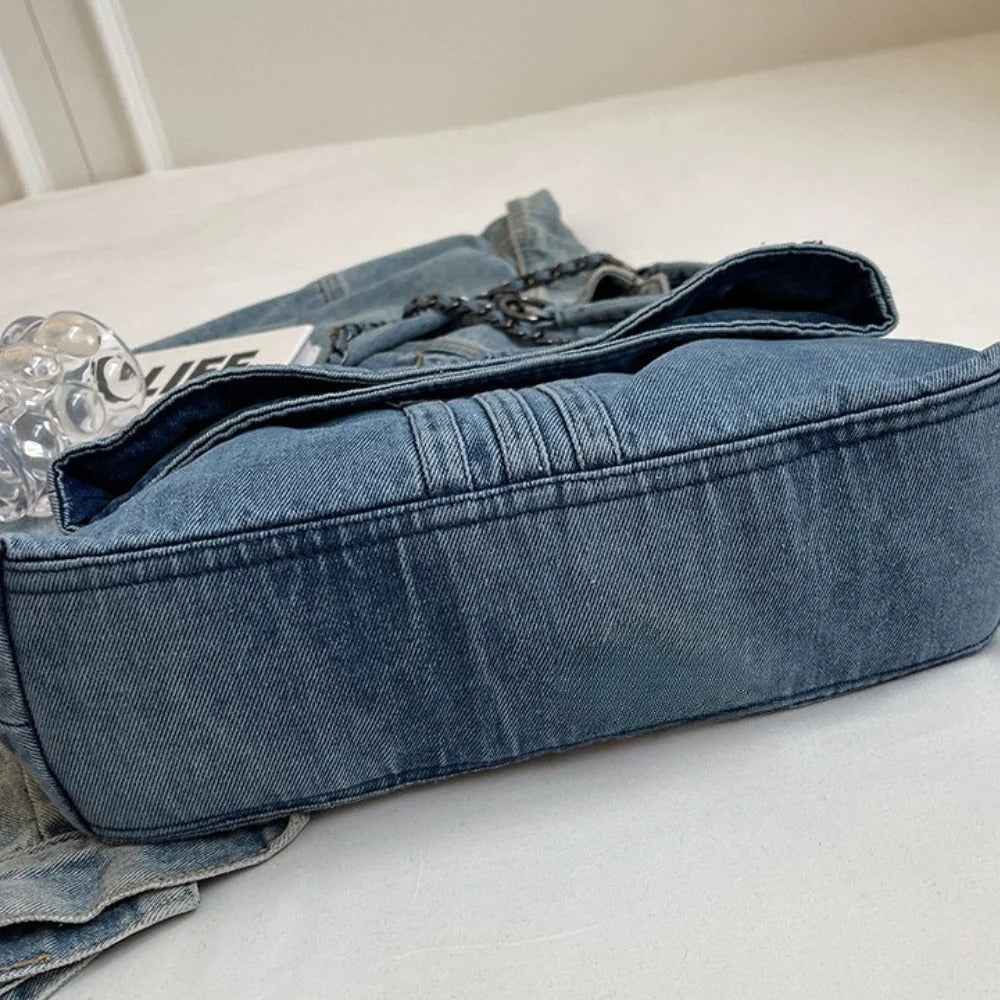 Base plate et large soufflet de la besace en denim posée sur un drap clair, rabat entrouvert