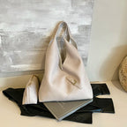 Duo beige rosé, grand sac et petite pochette alignés devant un panneau peint gris clair