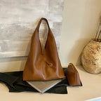 Cuir végan cognac grainé, sac et pochette posés sur un livre, près d'un vase texturé