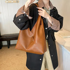 Silhouette en veste noire tenant le hobo cognac à l'épaule, sac largement ouvert sur le haut