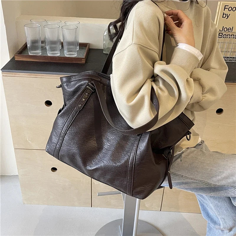 Bandoulière sur l'épaule, le sac brun café repose contre un sweat beige oversize