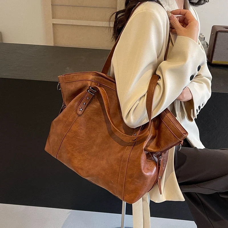 Cabas bowling marron porté sous le bras sur un blazer crème, poignées tenues à la main