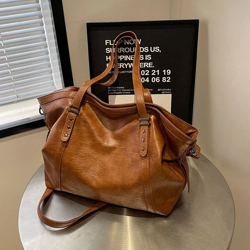 Marron cognac lustré, le sac posé de trois quarts sur une table ronde en métal brossé