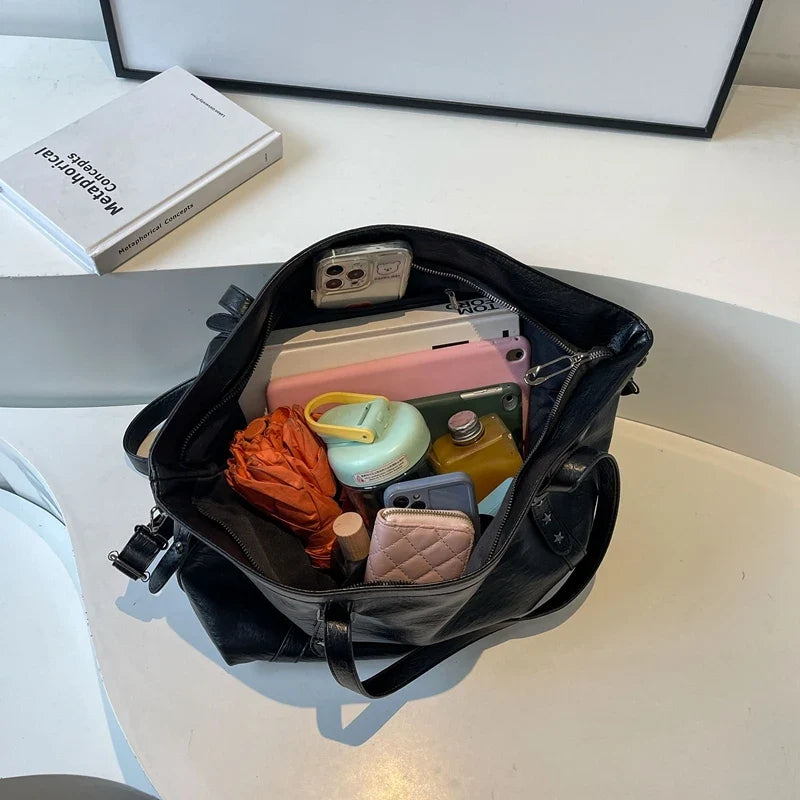 Intérieur ouvert du sac noir, garni d'un téléphone, d'une tablette, d'une trousse et d'un portefeuille