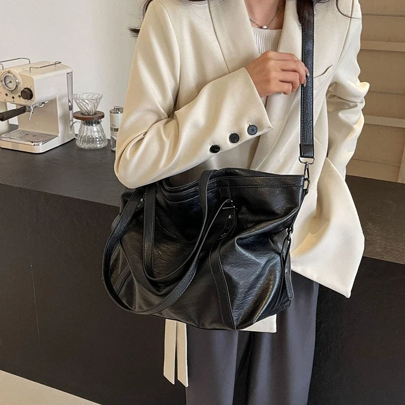 Porté à l'épaule sur un blazer crème, le sac bowling noir s'affaisse avec souplesse
