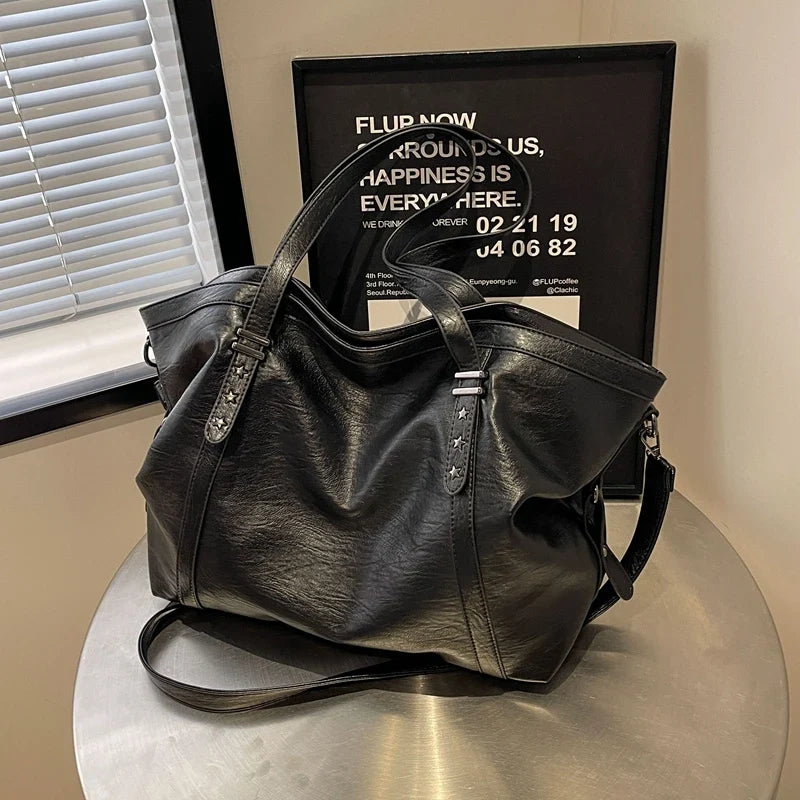 Cuir végan noir lustré, sac posé sur une table ronde métallique devant un cadre mural