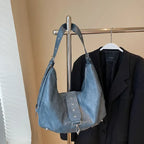 Suspendu à un portant à côté d'un blazer noir, le sac bleu gris laisse voir sa sangle amovible
