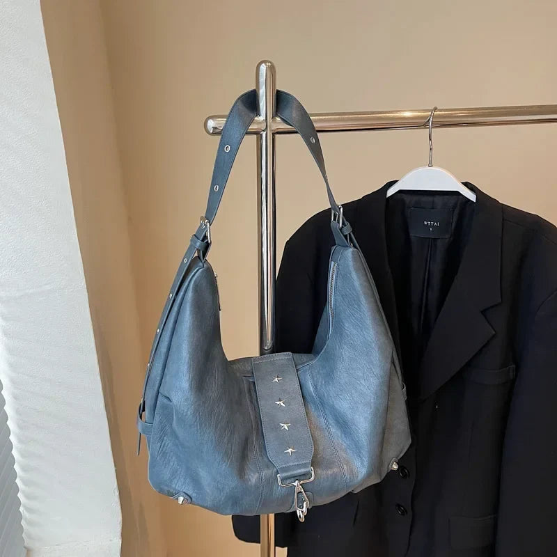 Suspendu à un portant à côté d'un blazer noir, le sac bleu gris laisse voir sa sangle amovible