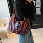 Version bordeaux portée à l'épaule sur un sweat noir et un jean large, sac écrasé sous le bras