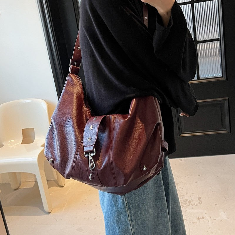 Version bordeaux portée à l'épaule sur un sweat noir et un jean large, sac écrasé sous le bras