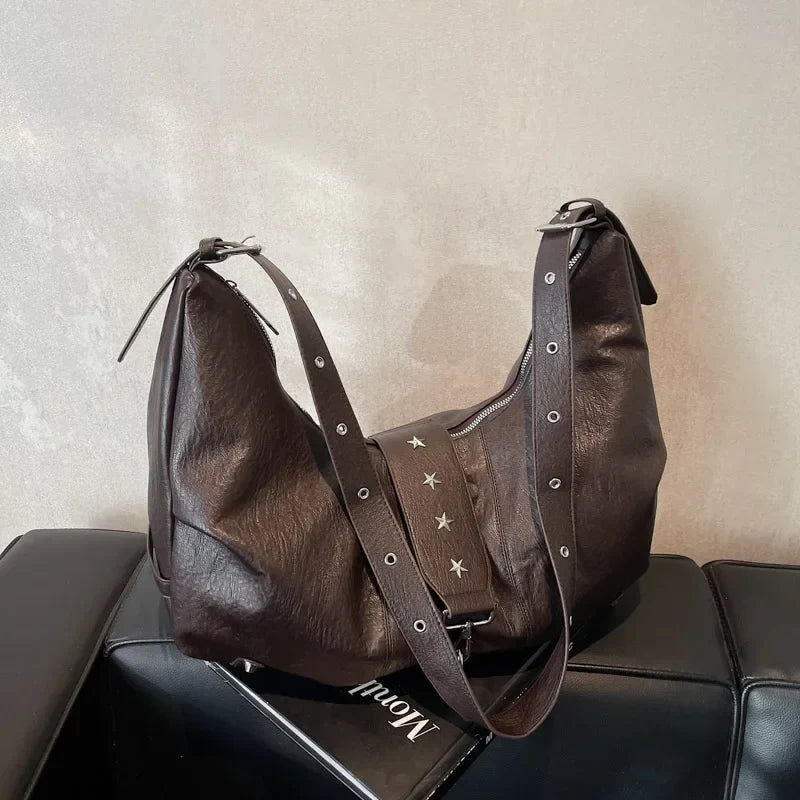Détail de la sangle amovible et de ses clous étoile sur le sac brun foncé posé sur un banc