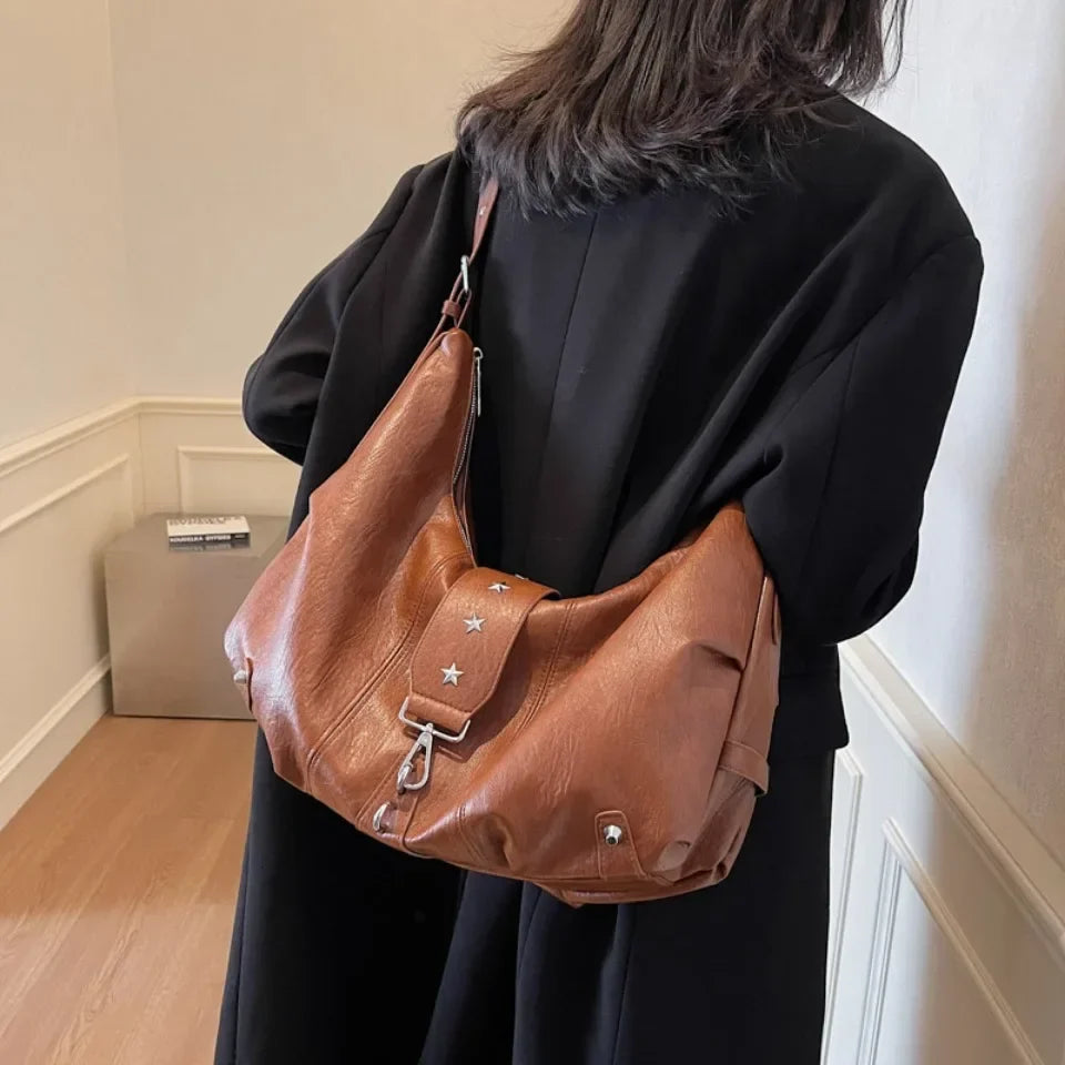 Silhouette de dos en manteau noir, le sac caramel remonté haut sous l'épaule, sangle large