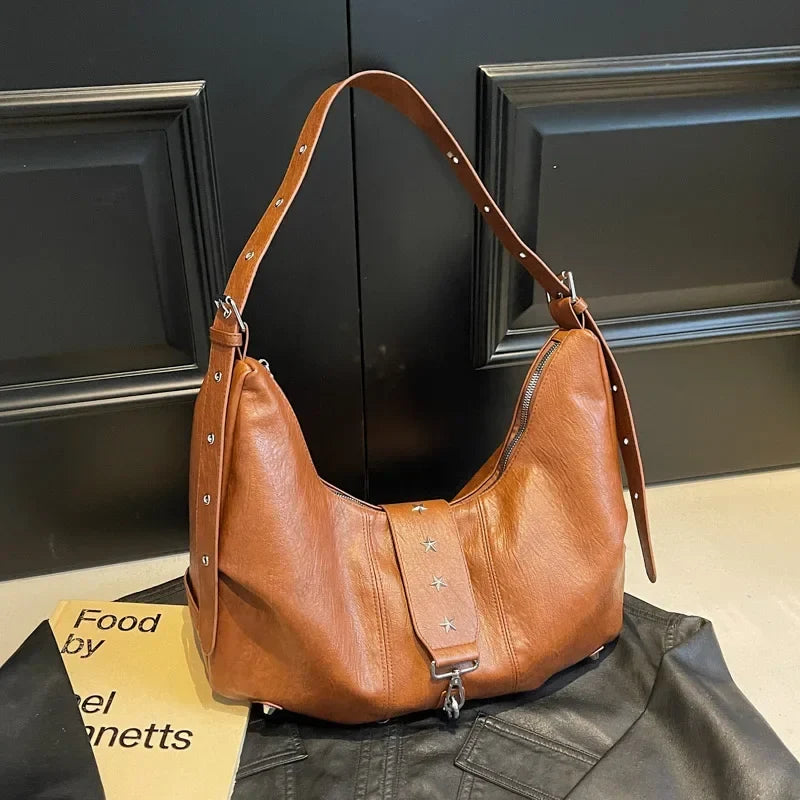 Caramel lustré et clous étoile, sac croissant posé de trois quarts près d'un livre et d'une veste
