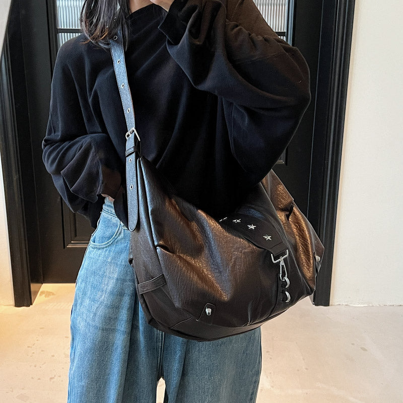 Croisé sur le torse, le sac brun foncé pend sur la hanche au-dessus d'un jean délavé