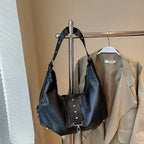 Accroché à un portant devant un trench beige, le sac noir montre sa sangle réglable cloutée