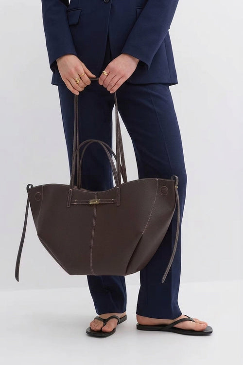 Tenu à deux mains devant un tailleur bleu marine, le cabas chocolat s'élargit vers le bas