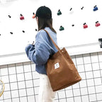 Épaule vêtue de jean supportant le tote bag marron, qui tombe librement le long de la hanche