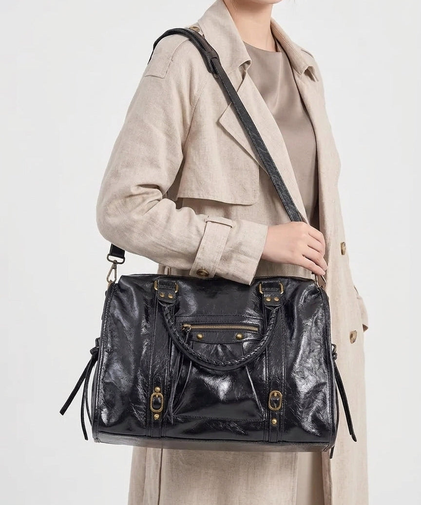 Femme en trench beige tenant le sac noir à bout de bras, bandoulière passée en travers du buste