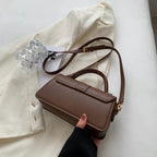 Trois quarts du sac chocolat tenu à la main, bandoulière déployée sur un blazer écru