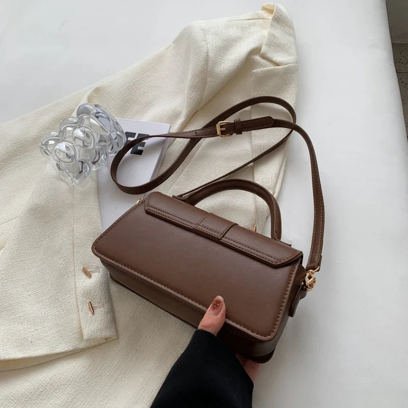 Trois quarts du sac chocolat tenu à la main, bandoulière déployée sur un blazer écru