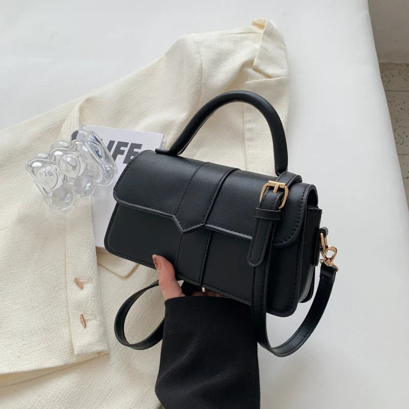 Version noire du sac tenue devant un blazer écru, boucle dorée et sangle d'épaule visibles