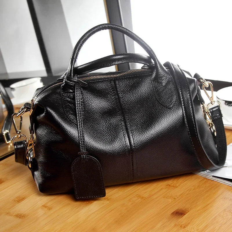 Posé sur une table en bois clair, le sac noir dévoile son zip ouvert et son mousqueton doré