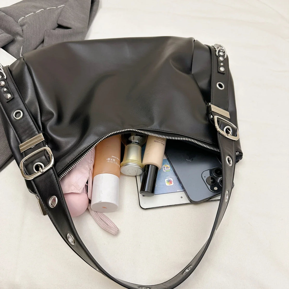 Ouverture zippée du sac noir, trousse rose, flacons de soin et téléphone glissés à l'intérieur